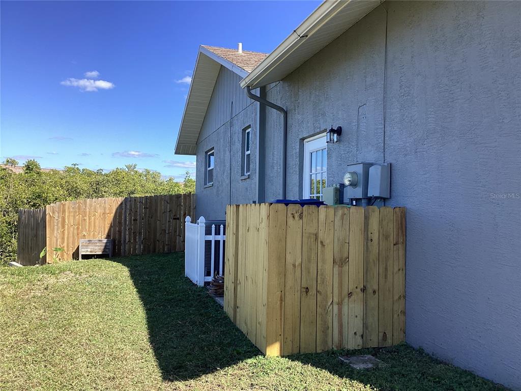 The exterior of a house features a wooden privacy fence, a white gate, and siding — 6426 DRAKE COURT, NEW PORT RICHEY, FL