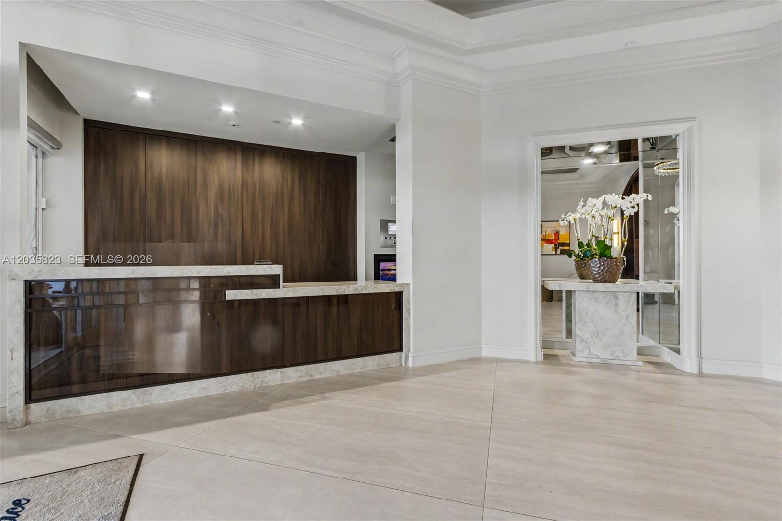 A modern reception area features a wood-paneled desk with marble accents and tile flooring — 3801 NE 207th St, Aventura FL 33180, AVENTURA, FL