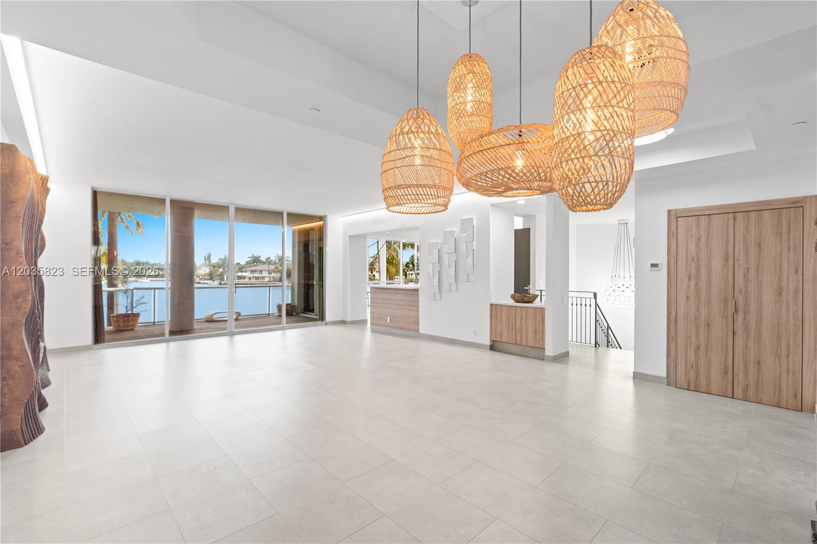 A spacious, minimalist living area features large windows, light tile floors, and woven pendant lights — 3801 NE 207th St, Aventura FL 33180, AVENTURA, FL