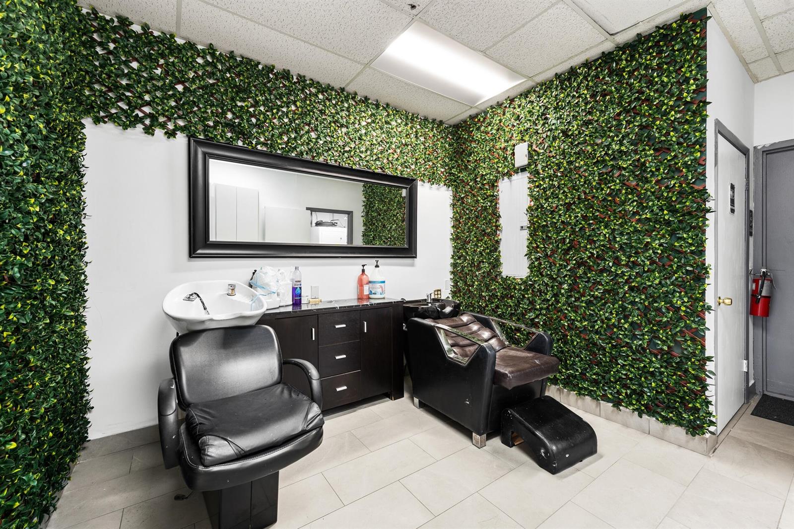A salon room features two shampoo chairs, a vanity, and walls covered in artificial greenery — 4608 South Jog Road, FL 33467, FL
