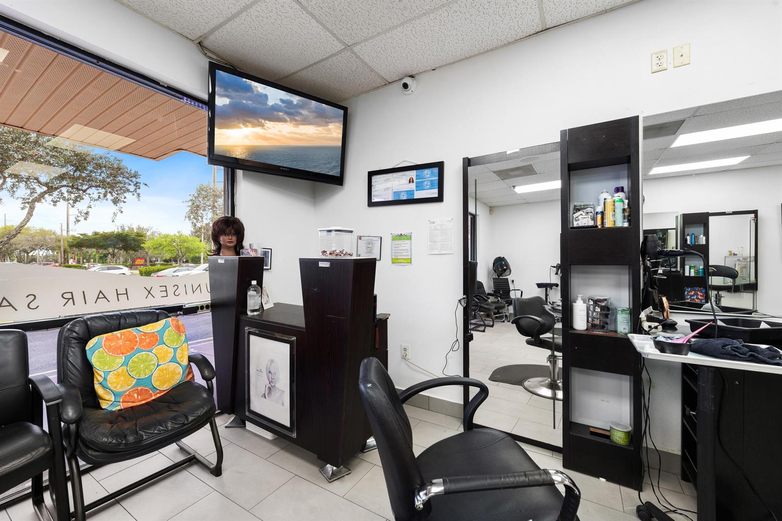A hair salon interior features styling chairs, a reception desk, mirrors, and a wall-mounted television — 4608 South Jog Road, FL 33467, FL