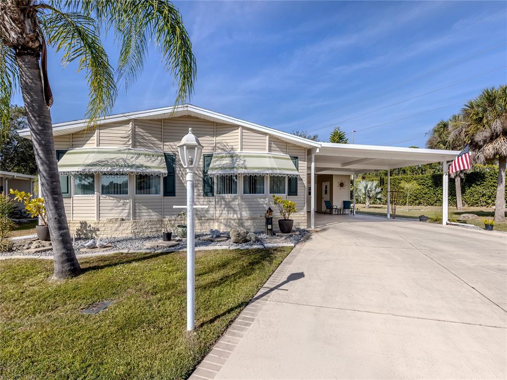 A single-story mobile home with beige siding, a carport, and striped window awnings — 236 NATURES WAY, NORTH PORT, FL