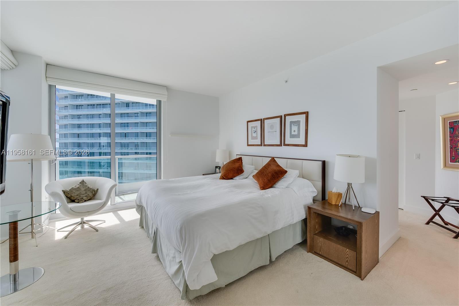 A bedroom features a bed, a white chair, and a large window overlooking a building — 1331 Brickell Bay Dr # 3311, Miami FL 33131, MIAMI, FL