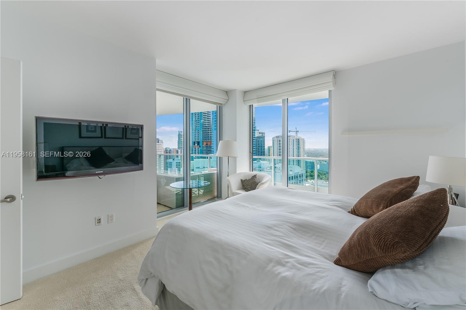 A bedroom features a bed, wall-mounted television, and floor-to-ceiling windows overlooking a city skyline — 1331 Brickell Bay Dr # 3311, Miami FL 33131, MIAMI, FL