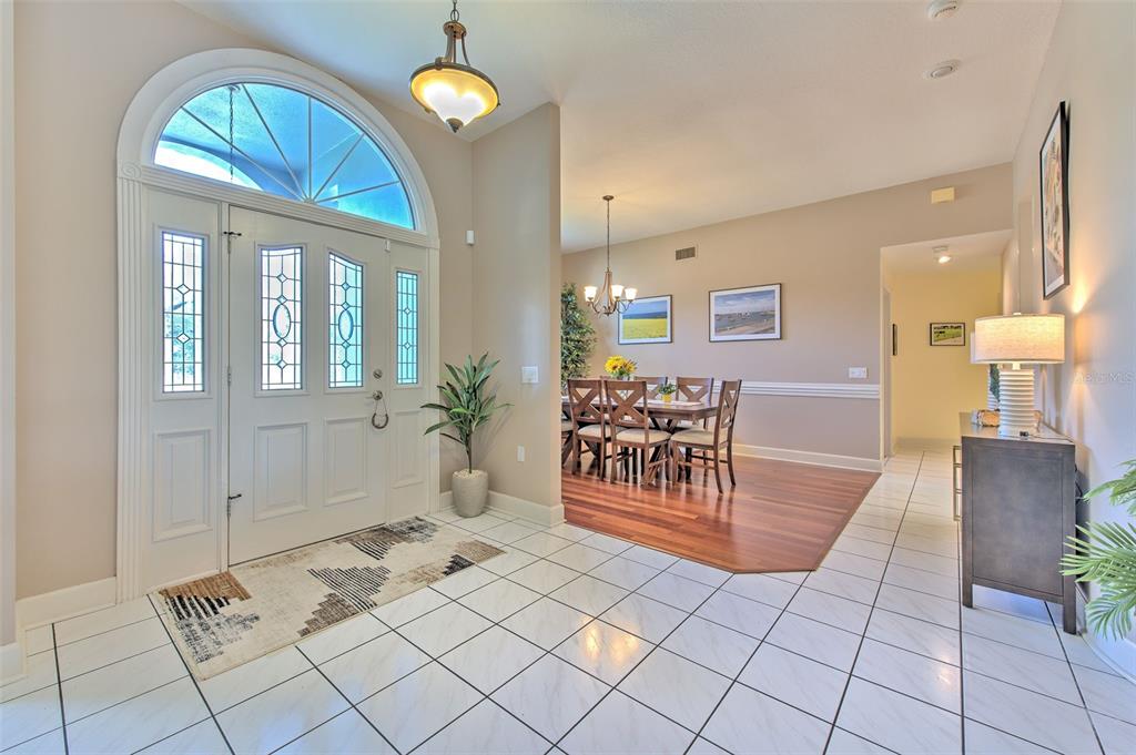 A bright foyer with white tile flooring leads into a dining room with hardwood floors — 5103 BROKEN SOUND LANE, VALRICO, FL