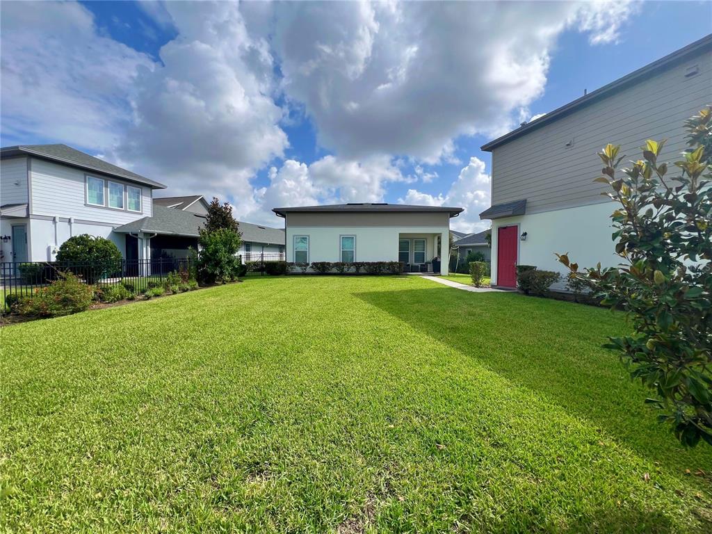 A grassy backyard sits between two houses under a blue sky with white clouds — 6958 BRIDGMAN STREET, ORLANDO, FL