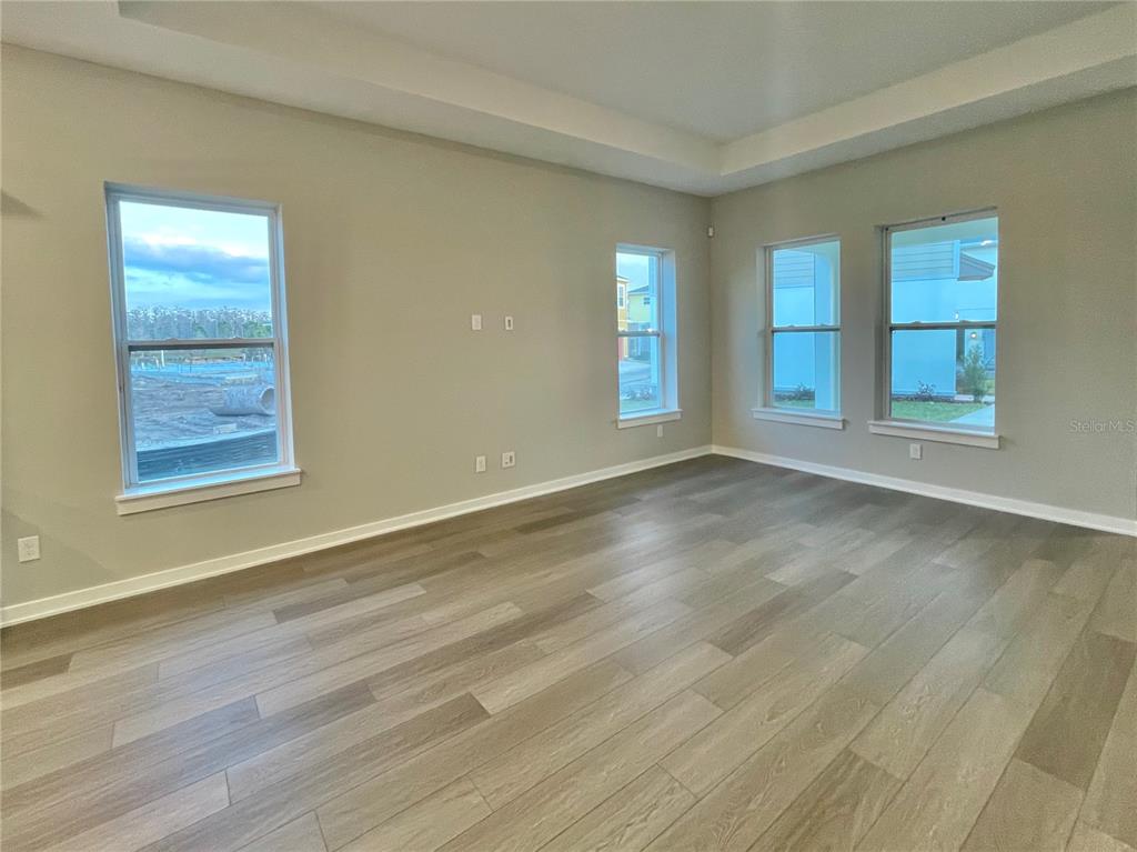 An empty living room features light-colored walls, wood-look flooring, and several windows — 6958 BRIDGMAN STREET, ORLANDO, FL