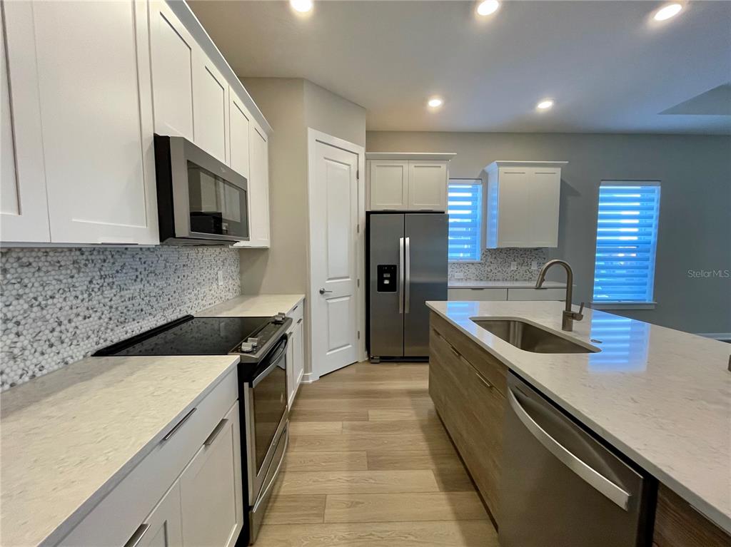 A modern kitchen features white cabinets, stainless steel appliances, a center island, and wood flooring — 6958 BRIDGMAN STREET, ORLANDO, FL