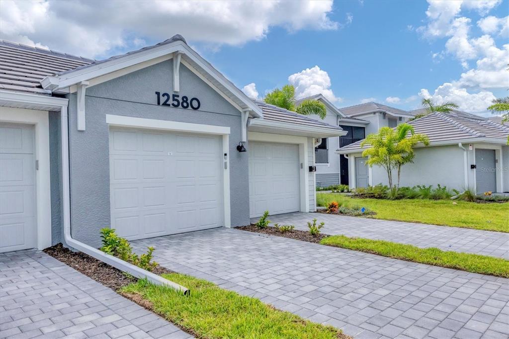 A gray suburban house exterior features a two-car garage and a paved driveway — 12580 GALAPAGOS COURT UNIT 108, VENICE, FL