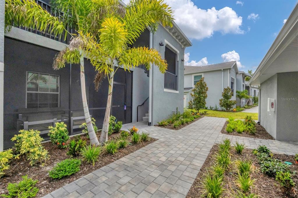 A paved walkway leads to the entrance of a gray multi-story building with landscaping — 12580 GALAPAGOS COURT UNIT 108, VENICE, FL