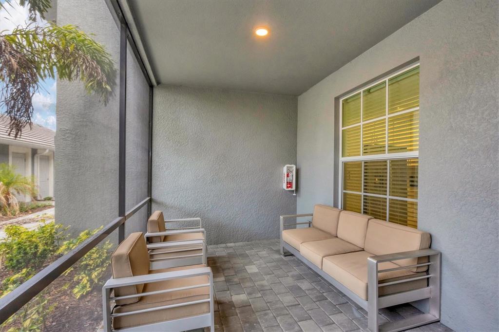 A screened-in patio features a paved floor, a sofa, two chairs, and a wall-mounted fire extinguisher — 12580 GALAPAGOS COURT UNIT 108, VENICE, FL