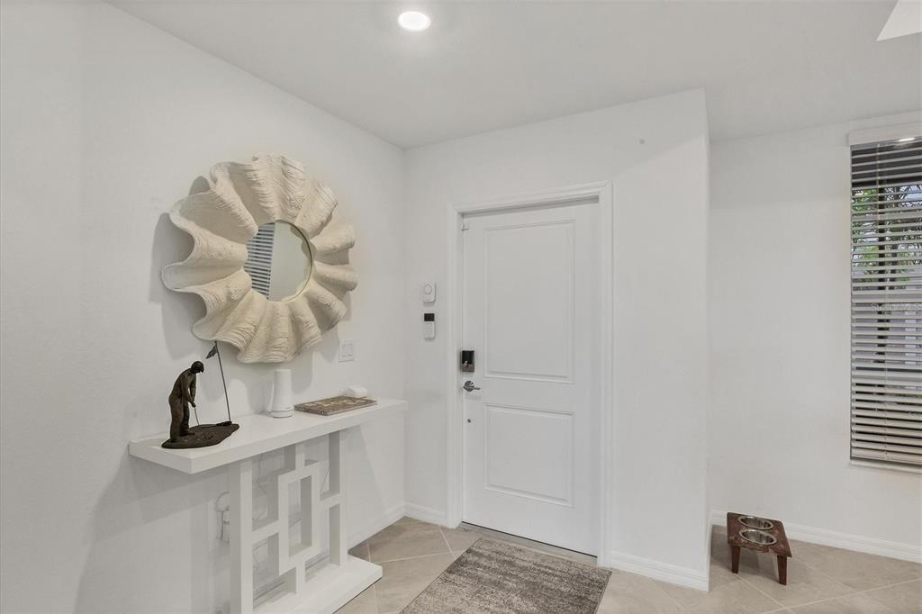 A white entryway features a shell-shaped mirror, a floating console table, and a front door — 12580 GALAPAGOS COURT UNIT 108, VENICE, FL