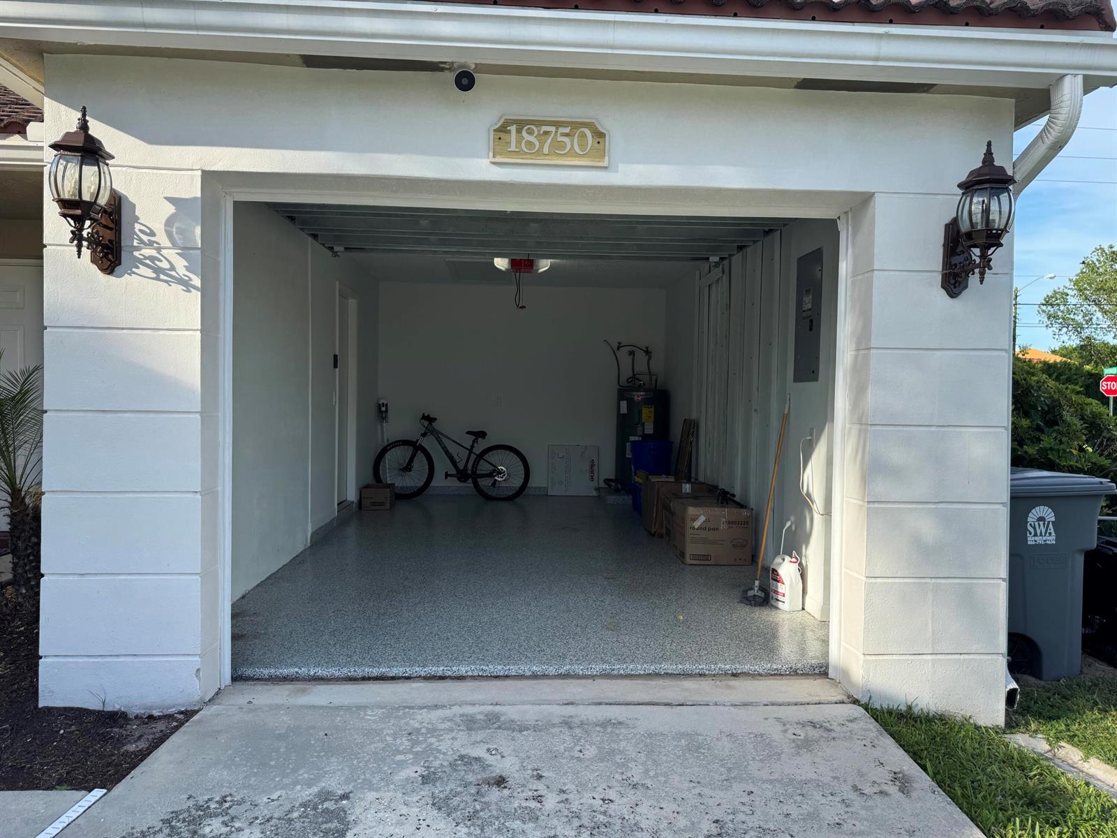 An open garage with a speckled epoxy floor, a bicycle, and storage boxes inside — 18750 Caspian Circle, Boca Raton FL 33496, BOCA RATON, FL