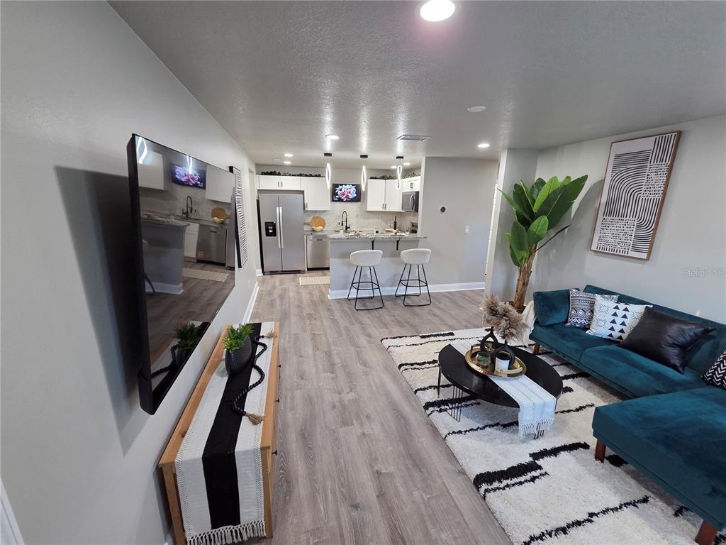 A modern living room features a teal sectional sofa, a large television, and an open kitchen — 1106 VALENCIA ROAD, PLANT CITY, FL