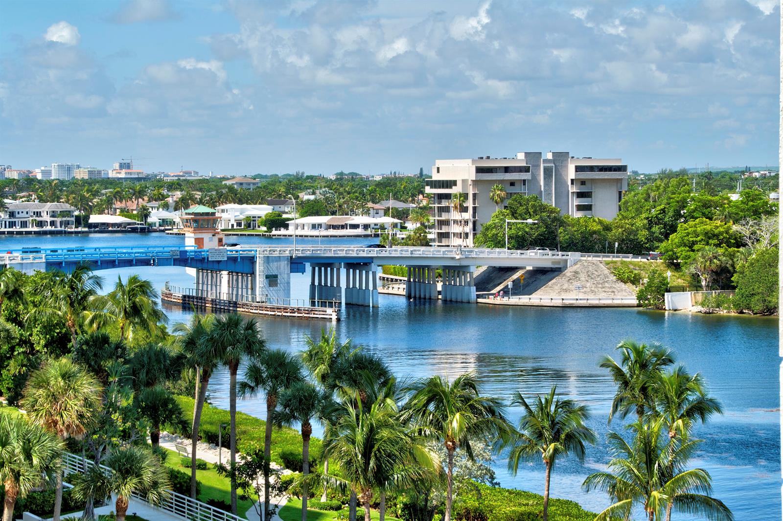 A bridge crosses a waterway surrounded by palm trees and buildings under a blue sky — BOCA RATON, FL