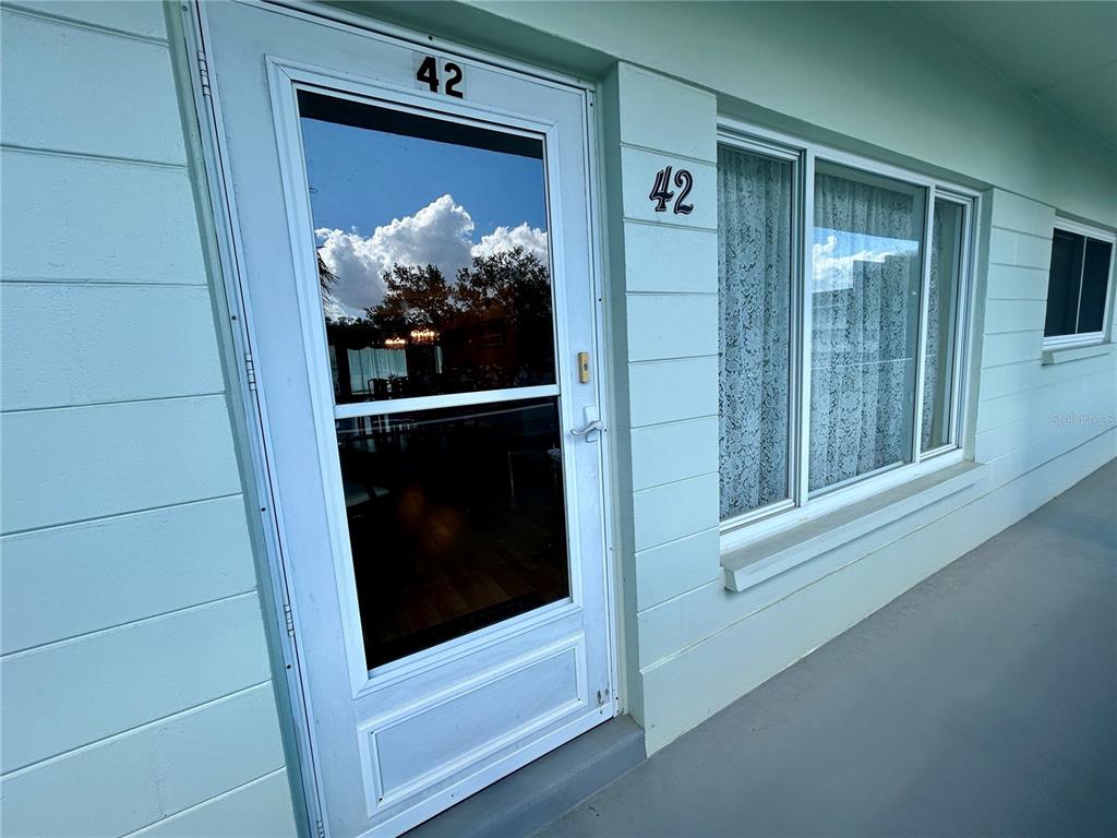 A light blue exterior wall features a white storm door and window marked with 42 — 2256 PHILIPPINE DRIVE UNIT 42, CLEARWATER, FL