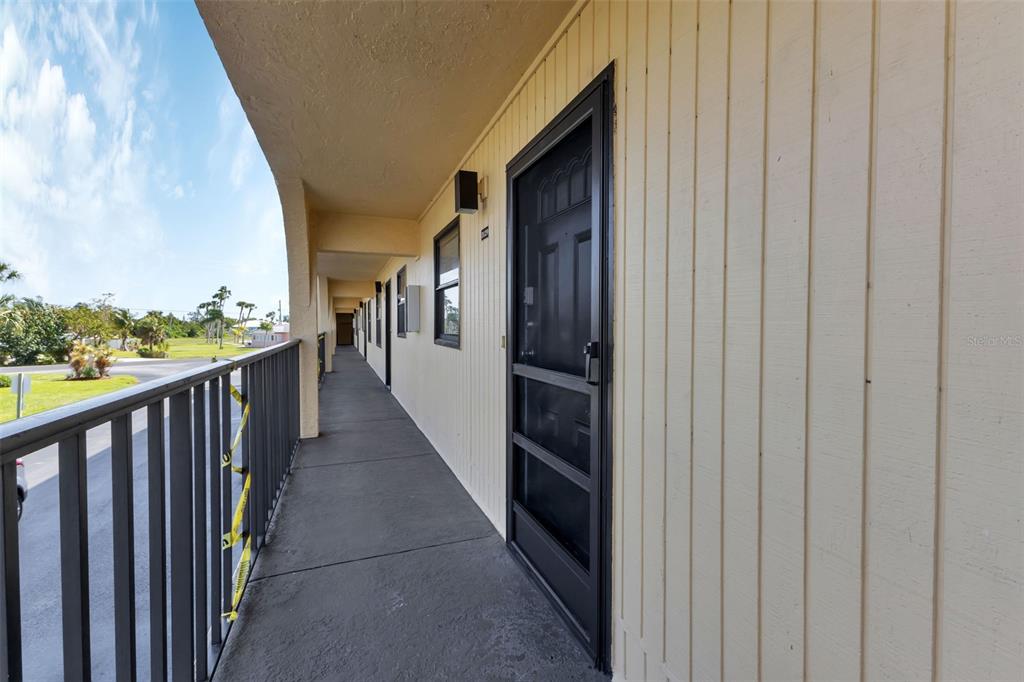 An exterior walkway with a metal railing and several apartment doors along a yellow wall — 14459 RIVER BEACH DRIVE UNIT 129, PORT CHARLOTTE, FL
