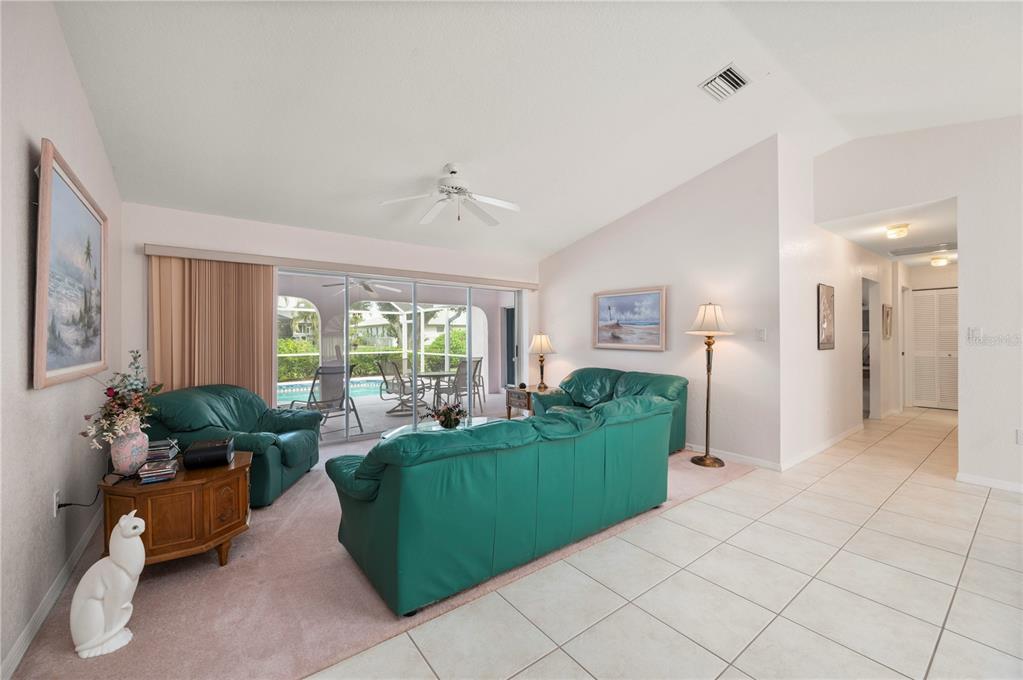 A living room with green leather furniture, pink carpeting, tile flooring, and sliding glass doors — 2231 HAMBURG LANE, PUNTA GORDA, FL