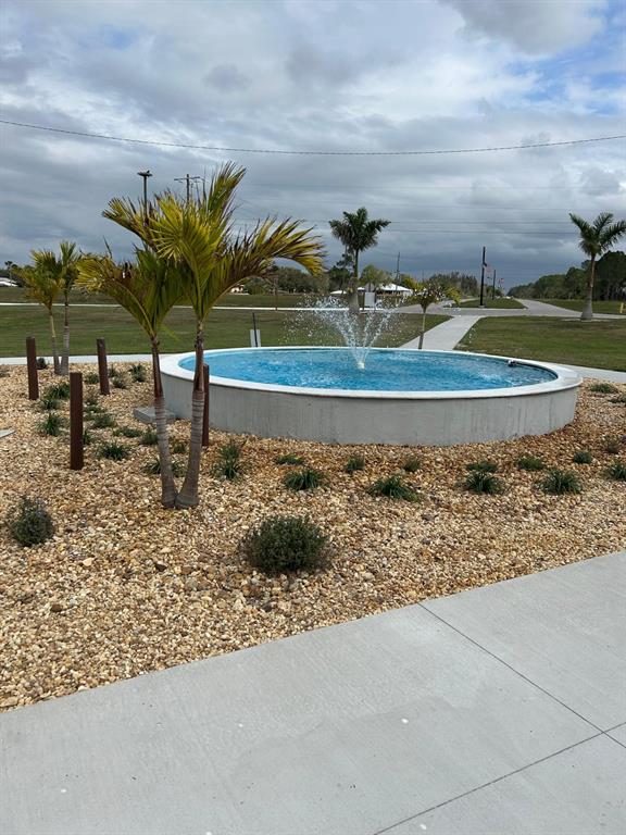 A circular water fountain sits in a landscaped area with palm trees and gravel mulch — 8 BOUGAINVILLE DRIVE, INDIAN LAKE ESTATES, FL