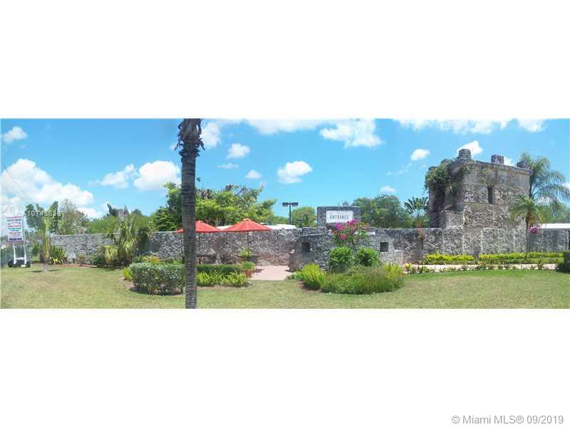 A stone wall and tower structure stand behind a grassy lawn with red patio umbrellas — SW 376TH ST, Homestead FL 33035, HOMESTEAD, FL