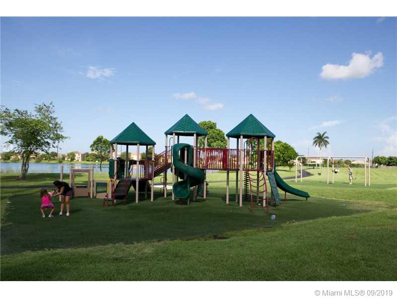 A playground with a multi-level structure and swings sits on a grassy field near water — SW 376TH ST, Homestead FL 33035, HOMESTEAD, FL