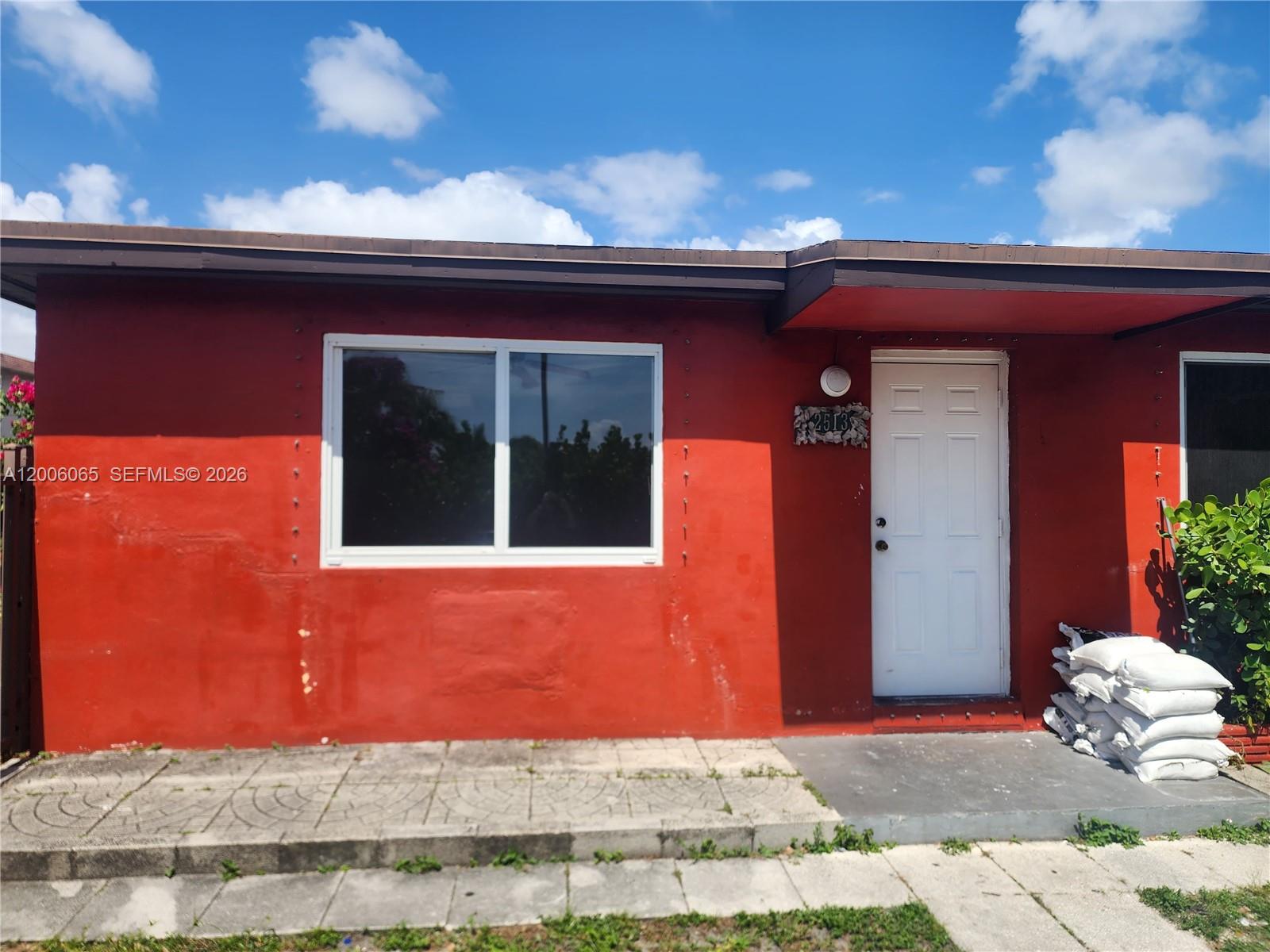 The exterior of a red house features a white front door and a large window — 2513 Lincoln St, Hollywood FL 33020, HOLLYWOOD, FL