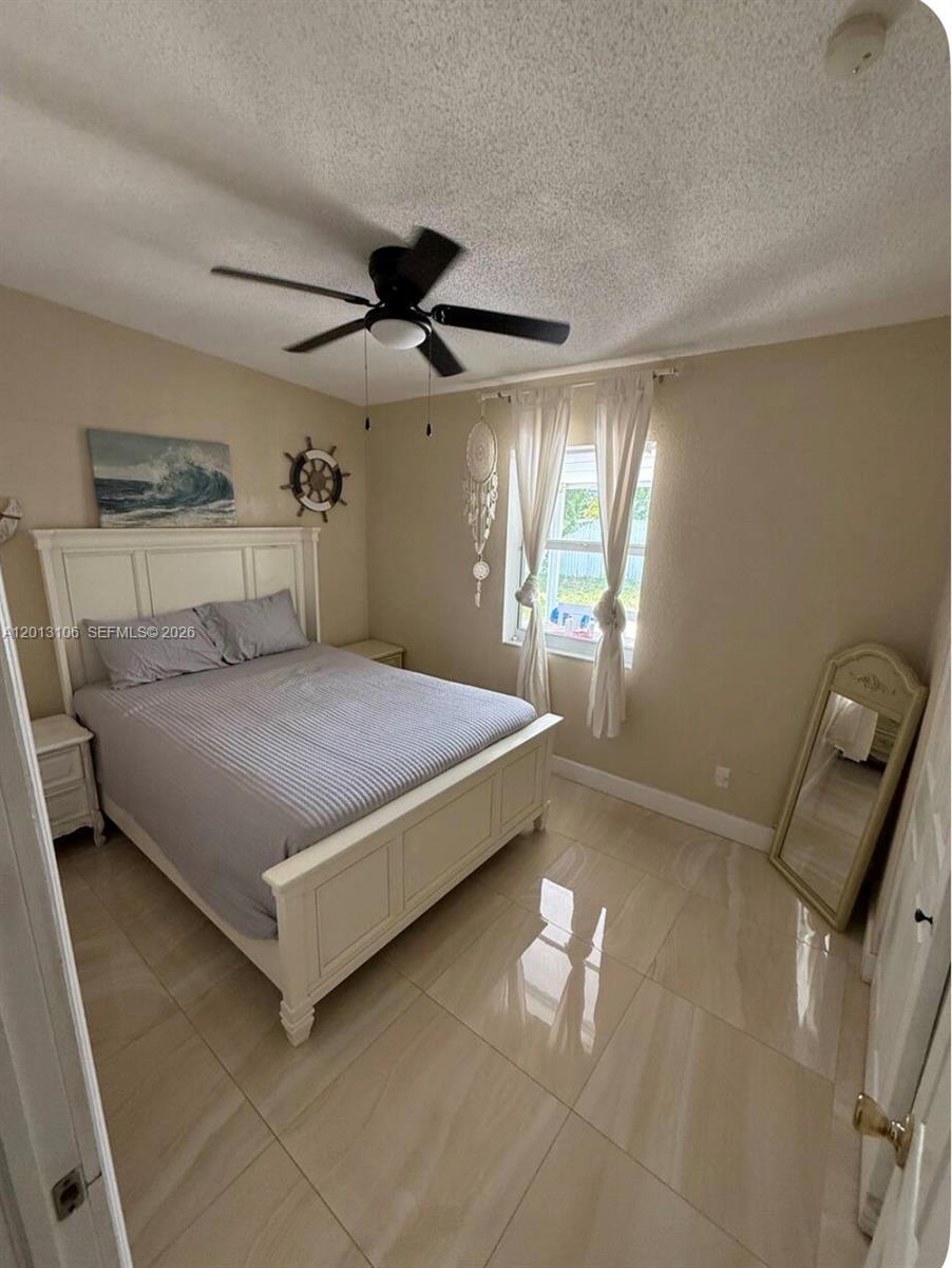 A bedroom features a white bed frame, tile flooring, a ceiling fan, and a floor mirror — 4720 NE 14th Ave, Pompano Beach FL 33064, POMPANO BEACH, FL