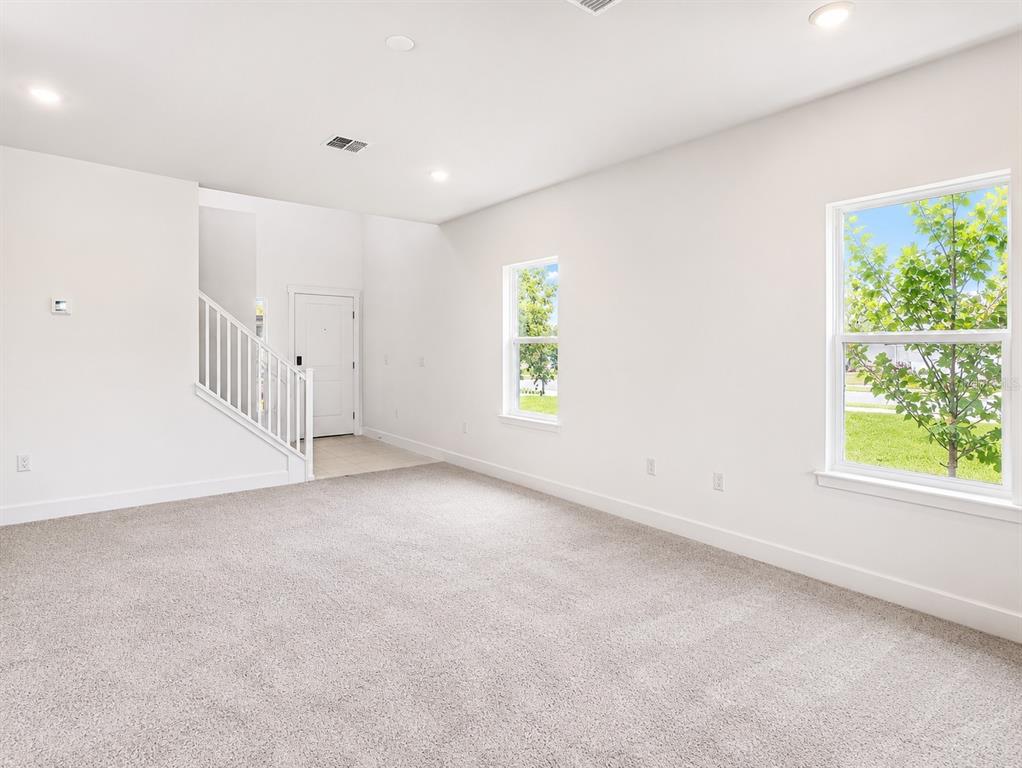 An empty living room with gray carpet, white walls, a staircase, and two windows — 7587 BENT TREE LOOP, ST CLOUD, FL