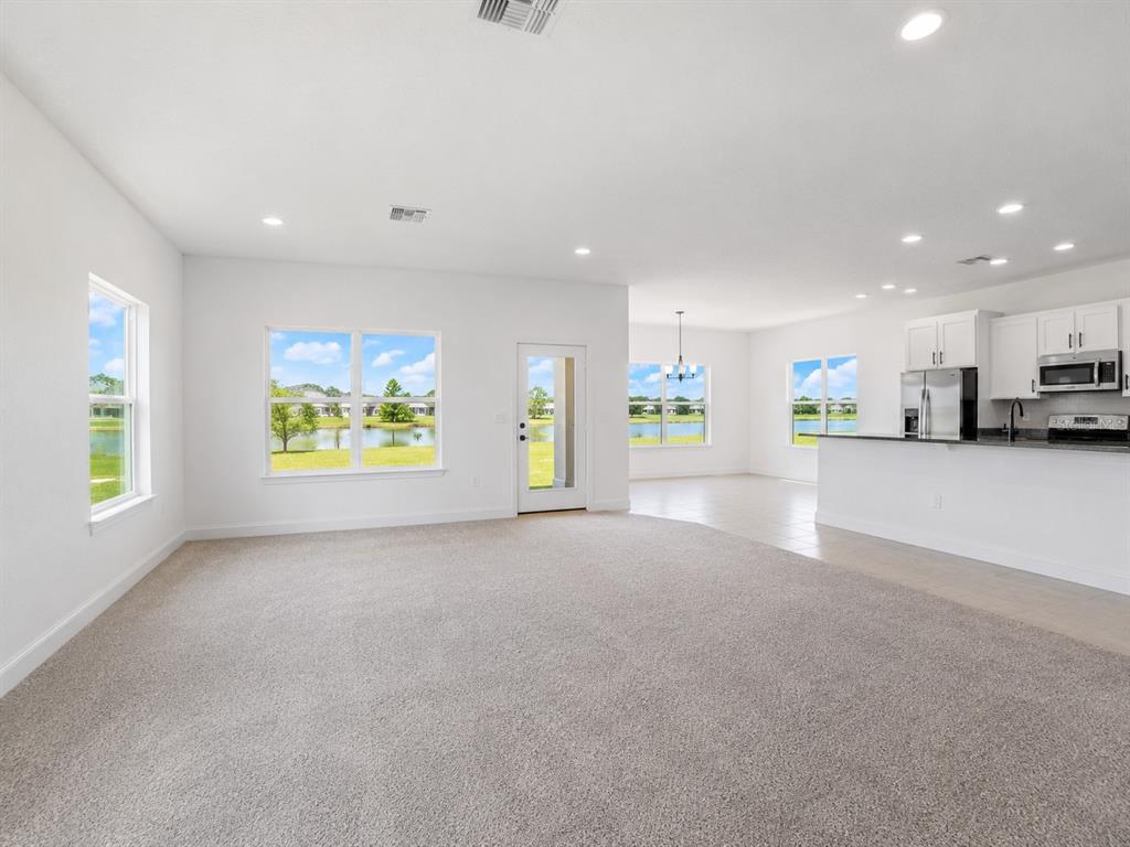 A spacious living room with carpeted floors opens to a kitchen and a lake view — 7587 BENT TREE LOOP, ST CLOUD, FL