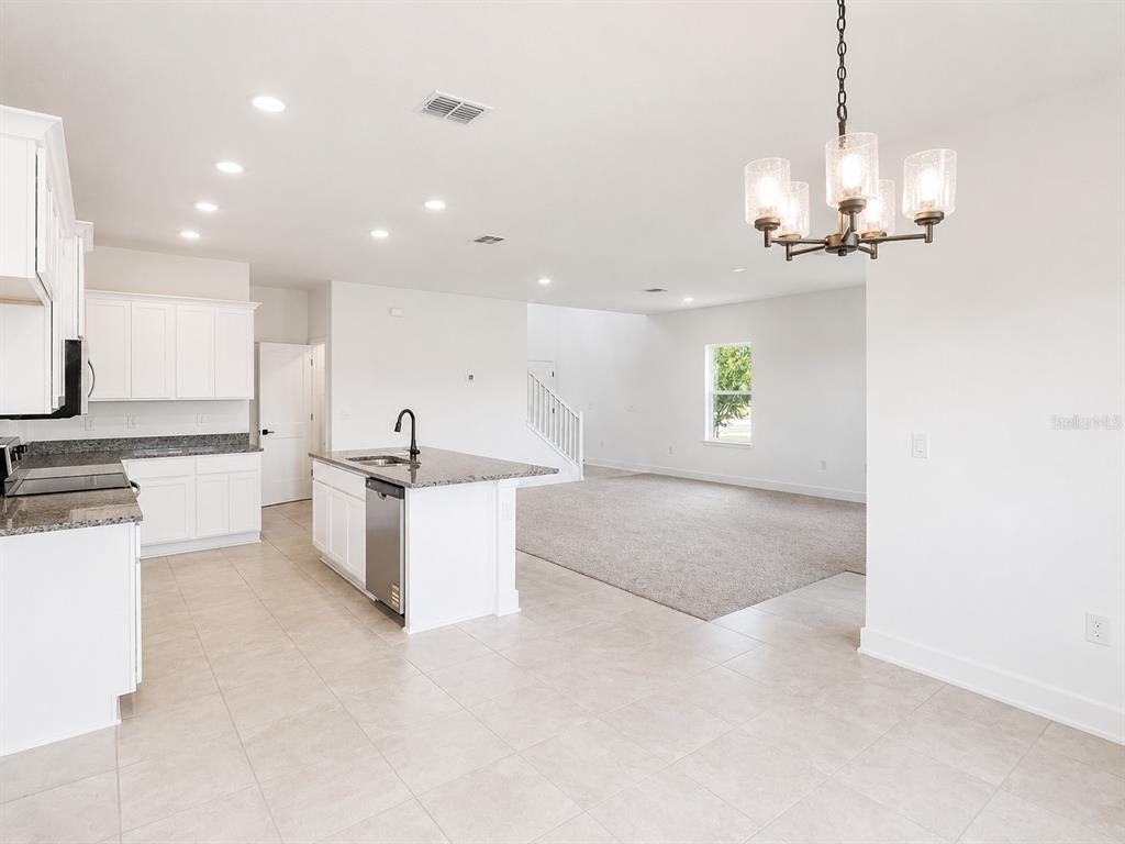 A kitchen with white cabinets and a granite island opens to a carpeted living area — 7587 BENT TREE LOOP, ST CLOUD, FL