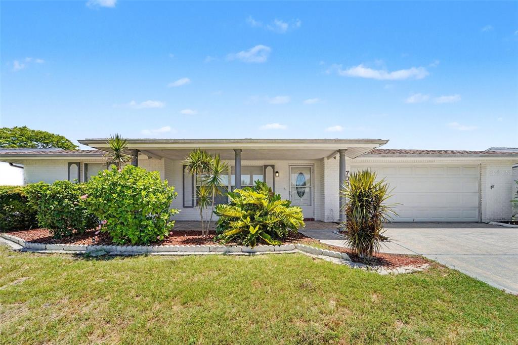 A single-story house with a white brick facade, a covered porch, and a two-car garage — 7006 MAPLEHURST DRIVE, PORT RICHEY, FL