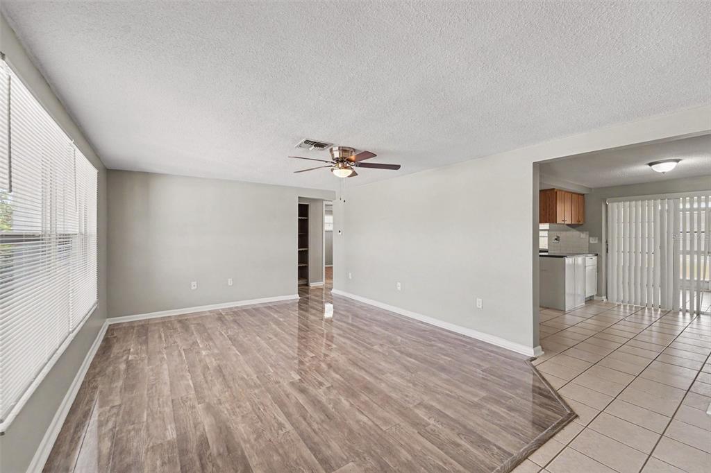 A living room with wood-look flooring transitions into a tiled dining area and kitchen — 7006 MAPLEHURST DRIVE, PORT RICHEY, FL