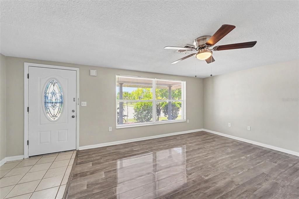 A living room with light gray walls, wood-look flooring, a ceiling fan, and a front door — 7006 MAPLEHURST DRIVE, PORT RICHEY, FL