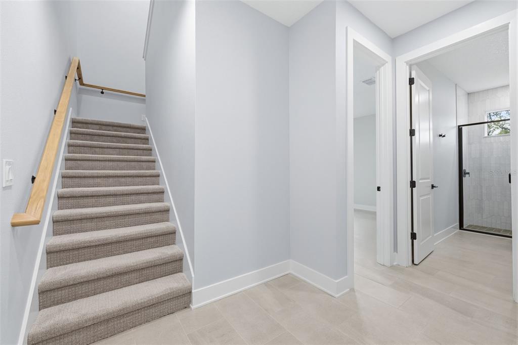A carpeted staircase with a wooden handrail sits beside a doorway leading to a bathroom — 4208 W CARMEN STREET UNIT D, TAMPA, FL