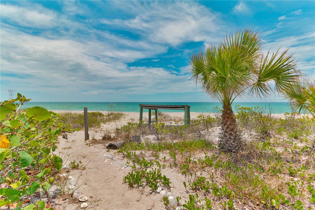 A sandy path leads through coastal vegetation toward a wooden structure on a sunny beach — 8300 MANASOTA KEY ROAD, ENGLEWOOD, FL