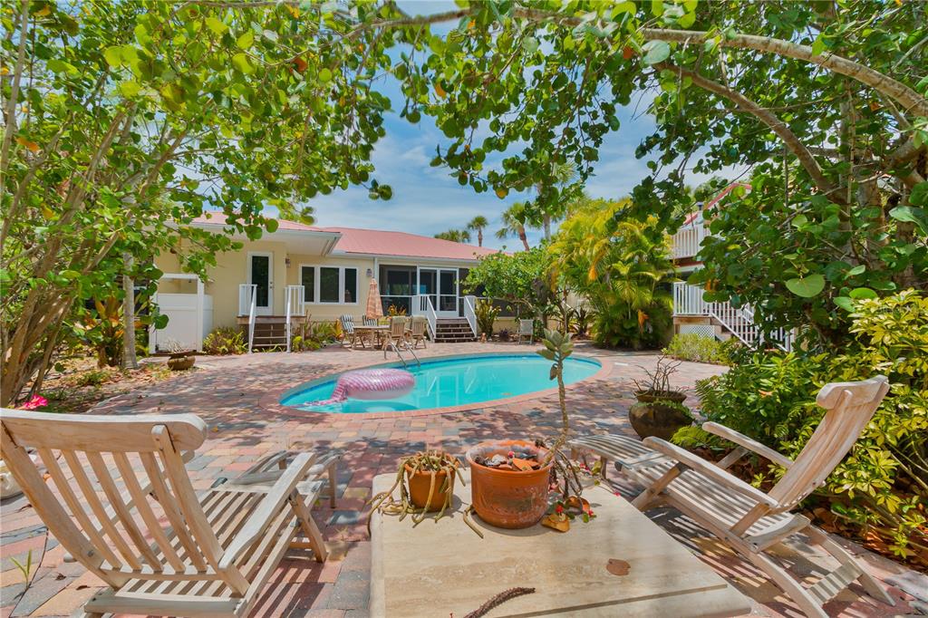 A backyard patio features a swimming pool, lounge chairs, and lush tropical landscaping — 8300 MANASOTA KEY ROAD, ENGLEWOOD, FL
