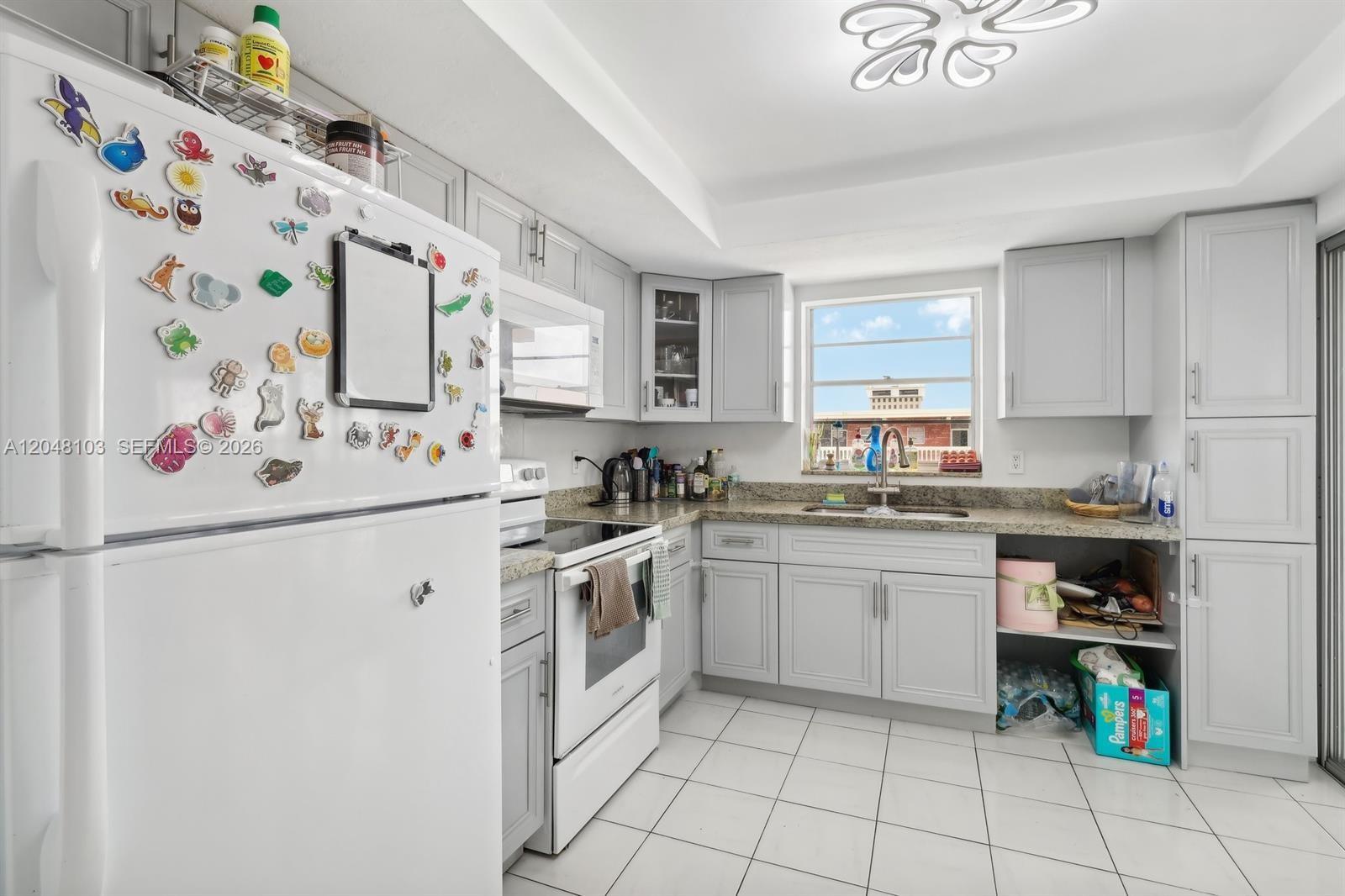 A kitchen features white cabinets, granite countertops, white appliances, and a window over the sink — HALLANDALE BEACH, FL