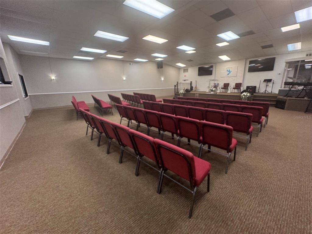 A church sanctuary features rows of red chairs facing a stage with musical equipment — 11601 S ORANGE BLOSSOM TRAIL UNIT 203, ORLANDO, FL