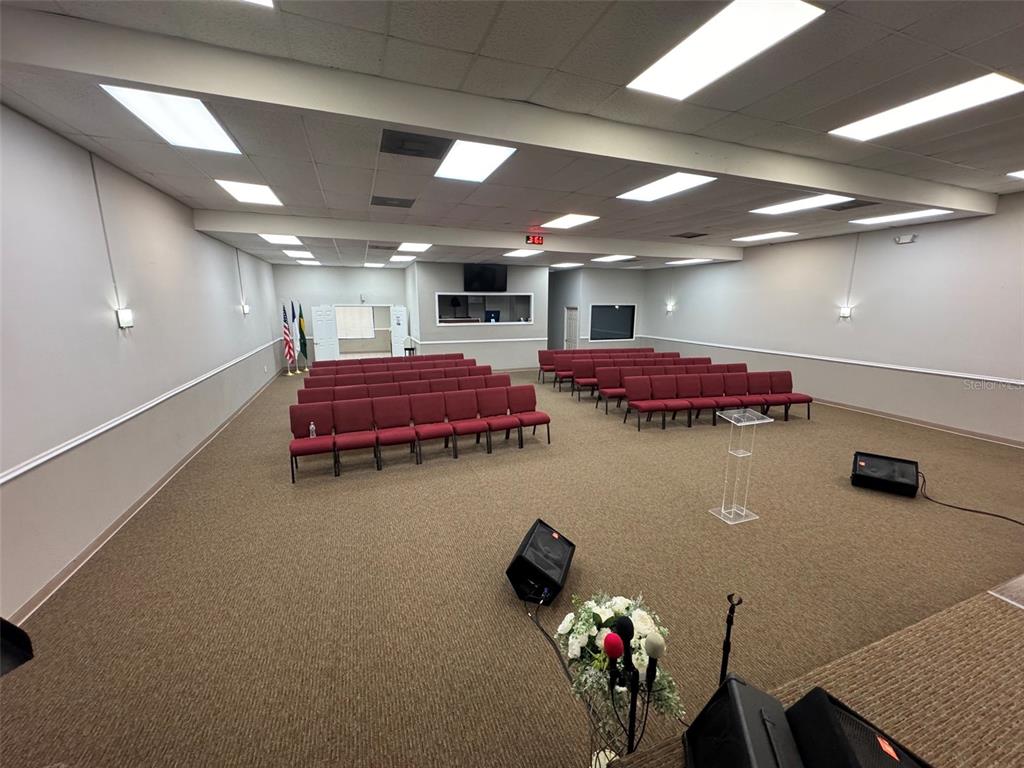 A large, carpeted meeting room features rows of red chairs and a clear podium — 11601 S ORANGE BLOSSOM TRAIL UNIT 203, ORLANDO, FL