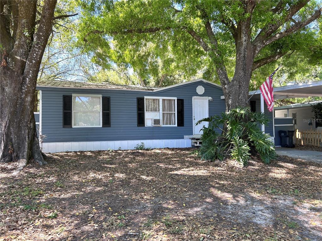 A blue single-story manufactured home sits under large trees with a front yard and carport — 10638 BAY HILLS CIRCLE, THONOTOSASSA, FL