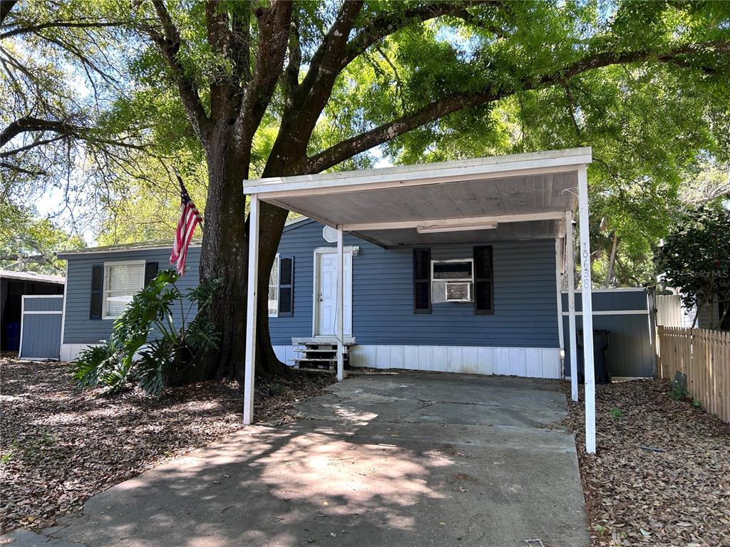 A blue single-story house features a front carport, a concrete driveway, and a large tree — 10638 BAY HILLS CIRCLE, THONOTOSASSA, FL