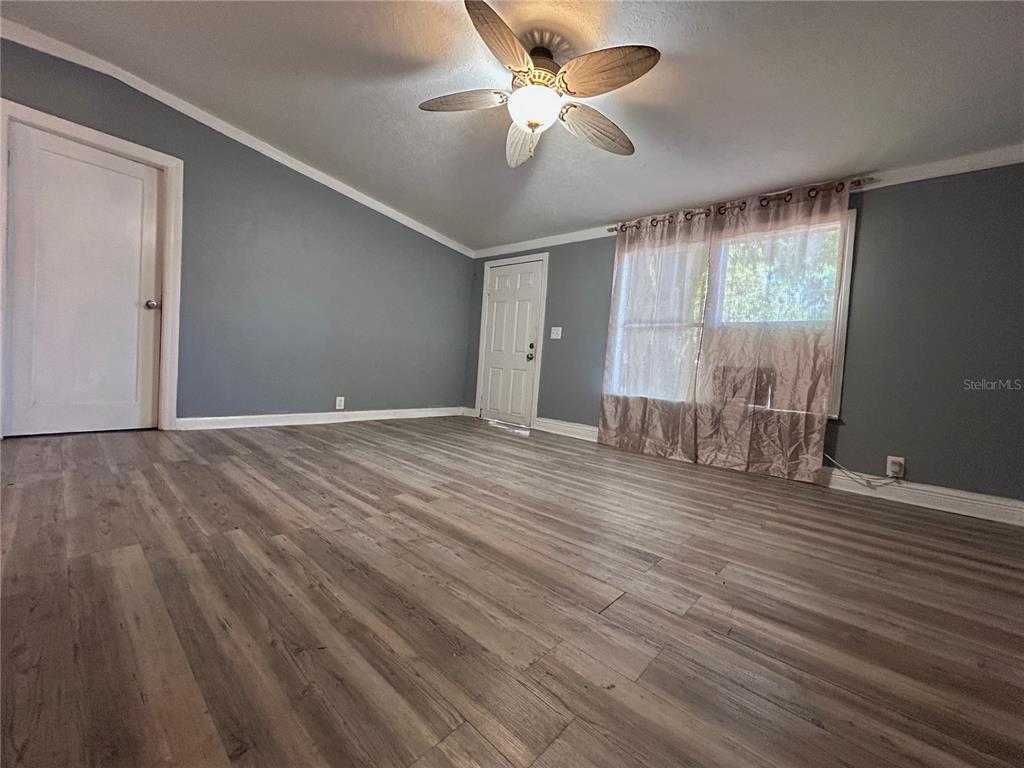 An empty room features gray walls, wood-look flooring, a ceiling fan, and a white door — 10638 BAY HILLS CIRCLE, THONOTOSASSA, FL
