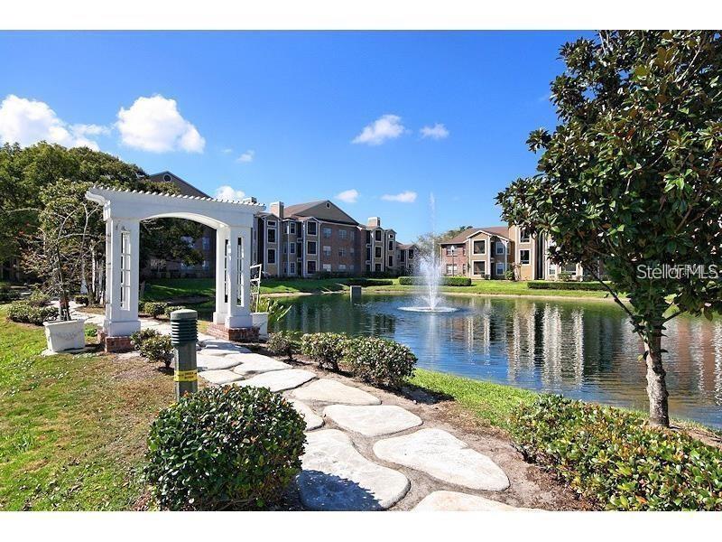 A stone path leads to a white pergola overlooking a pond with a fountain — 4400 THORNBRIAR LANE UNIT A202, ORLANDO, FL