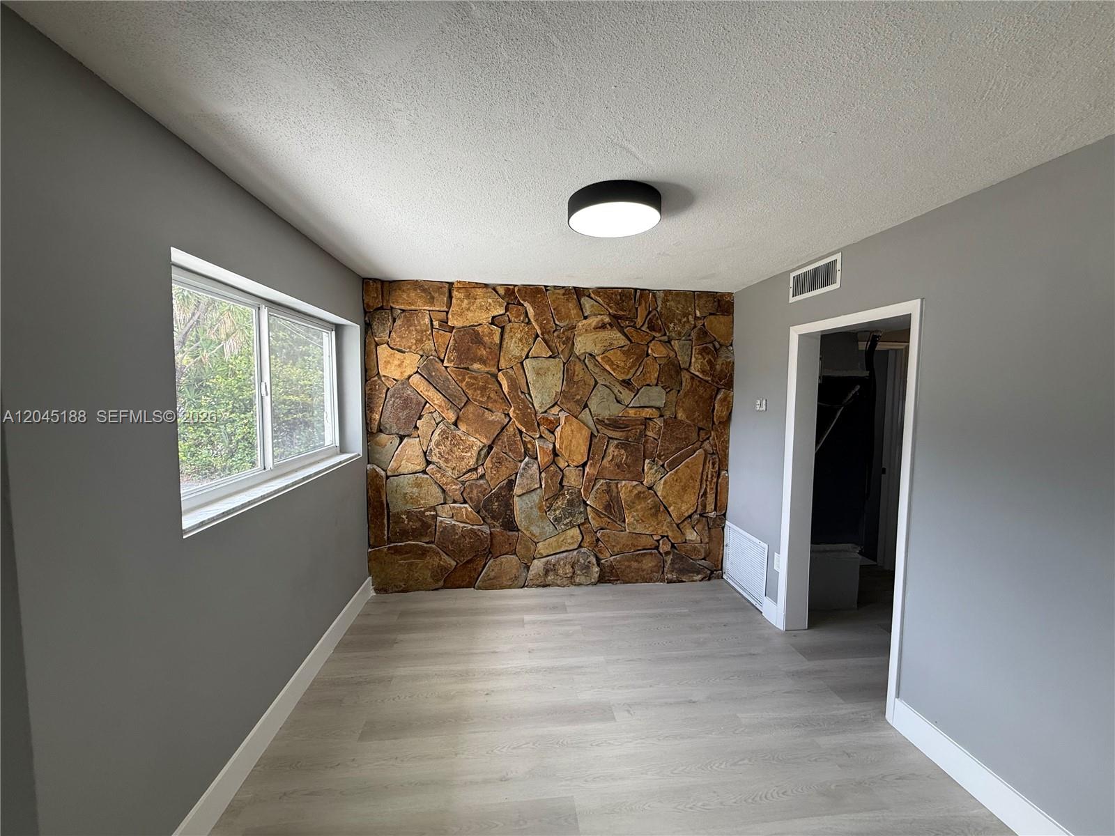 A room features gray walls, light wood-look flooring, and a prominent stone accent wall — 17880 NE 13th Ave, North Miami Beach FL 33162, NORTH MIAMI BEACH, FL