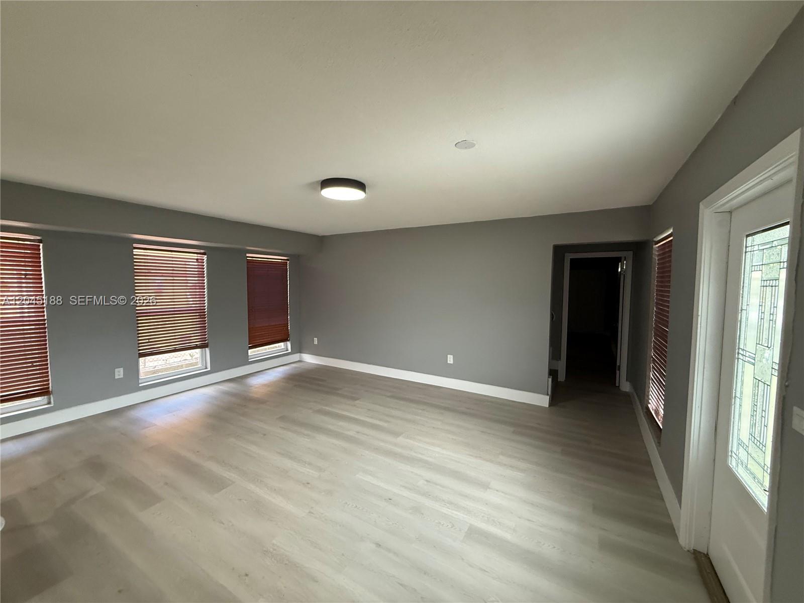 A living room features gray walls, light wood-look flooring, three windows, and a glass-paneled door — 17880 NE 13th Ave, North Miami Beach FL 33162, NORTH MIAMI BEACH, FL