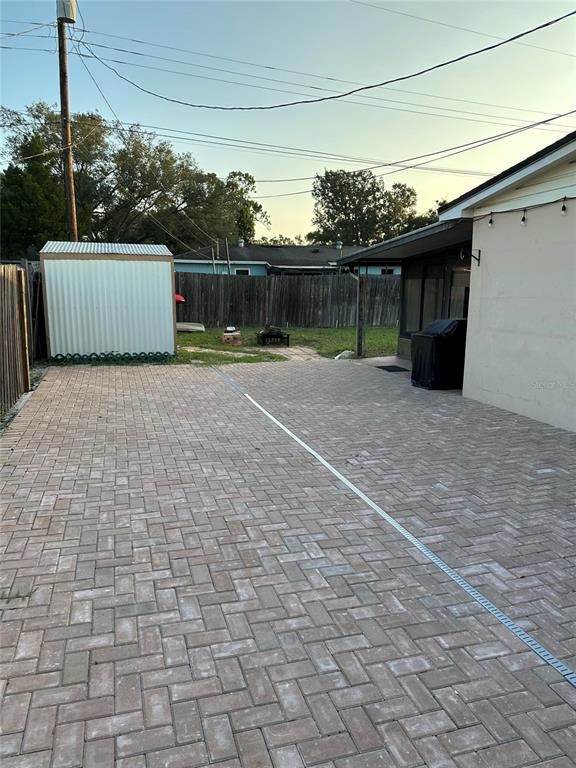 A paved patio area features a metal storage shed and a covered porch with a grill — 522 WILSHIRE DRIVE, CASSELBERRY, FL
