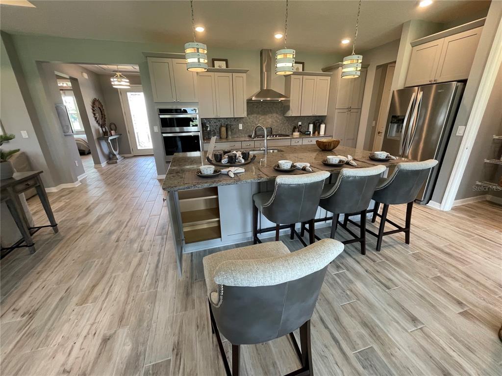 A kitchen features a granite-topped island with bar seating, stainless appliances, and light wood flooring — 9152 SW 85TH PLACE, OCALA, FL