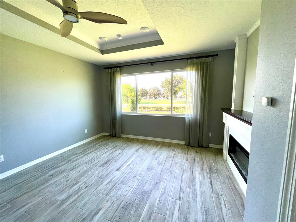 A living room features wood-look tile flooring, a tray ceiling with a fan, and a fireplace — 9152 SW 85TH PLACE, OCALA, FL