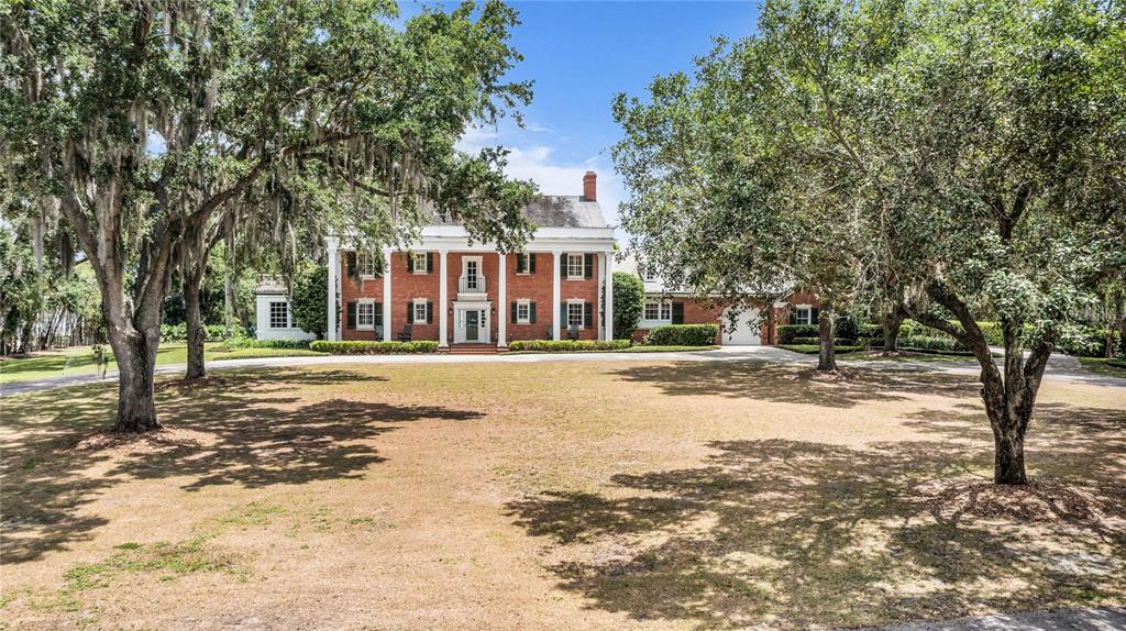 A large, two-story brick colonial-style house sits behind a wide lawn with mature trees — 1530 WATERWITCH DRIVE, ORLANDO, FL