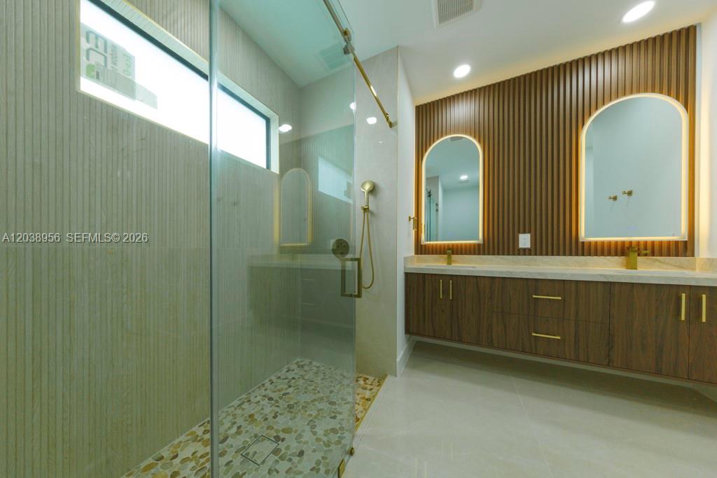 A modern bathroom features a glass-enclosed shower, a double vanity, and wood-slat wall paneling — 814 Calyton Ave, Lehigh Acres FL 33972, LEHIGH ACRES, FL